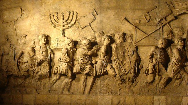 Arch of Titus Menorah: This photograph shows a modern replica of the Arch of Titus relief depicting the spoils of the Jerusalem Temple, including the temple menorah, carried in a t