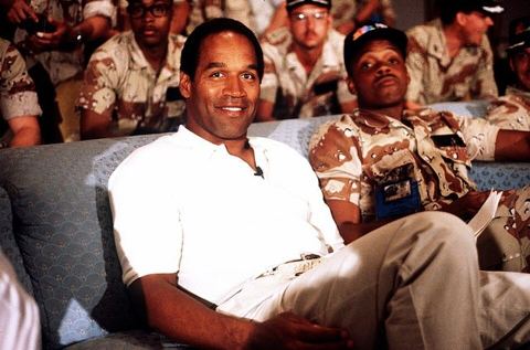 O.J. Simpson 1990 · DN-ST-91-03444: NBC Sports commentator and former professional football player O. J. Simpson sits with a group of servicemen to watch a Thanksgiving Day footbal